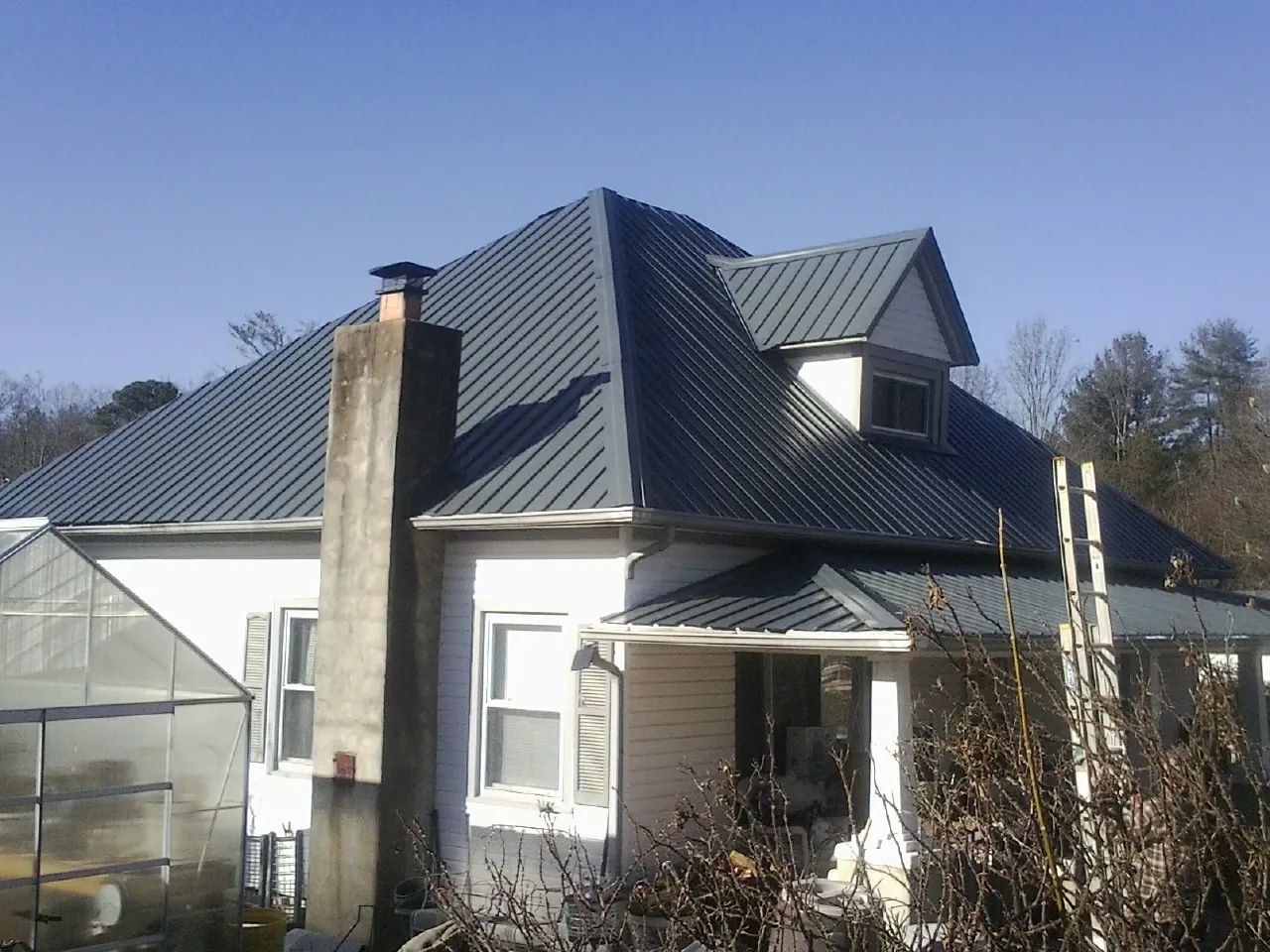Dark blue standing seam metal roof on a white farmhouse with dormer — Slate & Tile Roof Repair by Roofing Brothers in Mattituck