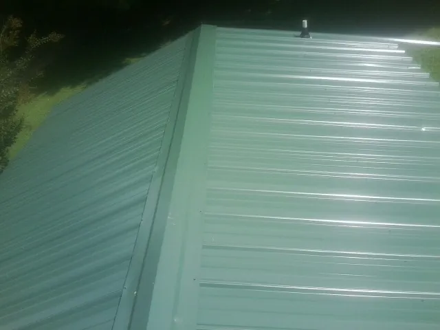 New green metal panels meeting at the ridge of a roof — Flat Roof Repair work by our crew in Mattituck