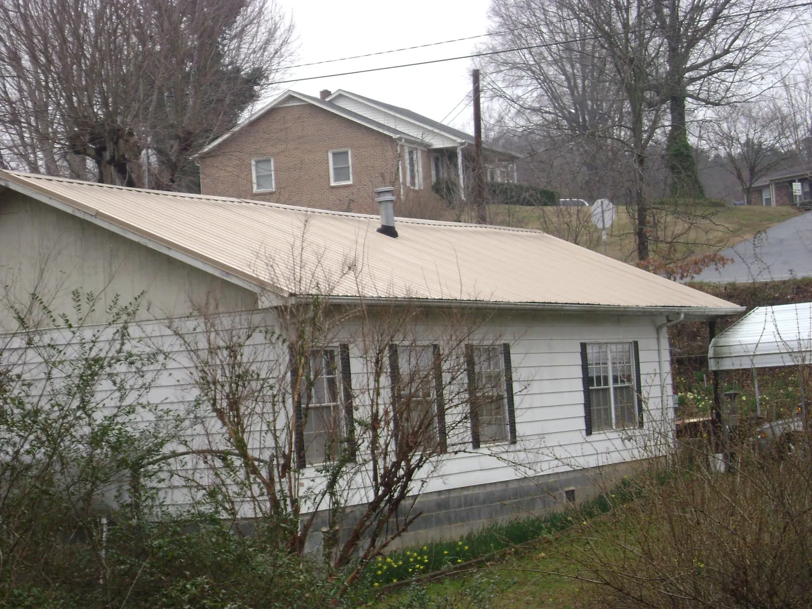 Tan metal roof on a white sided house set into a hillside — Commercial Roofing by Roofing Brothers in Mattituck